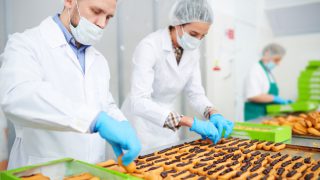 Confectionery factory workers in white coats making pastry with chocolate