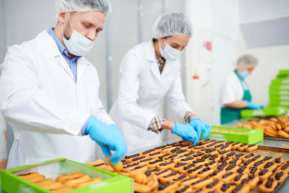 Confectionery factory workers in white coats making pastry with chocolate