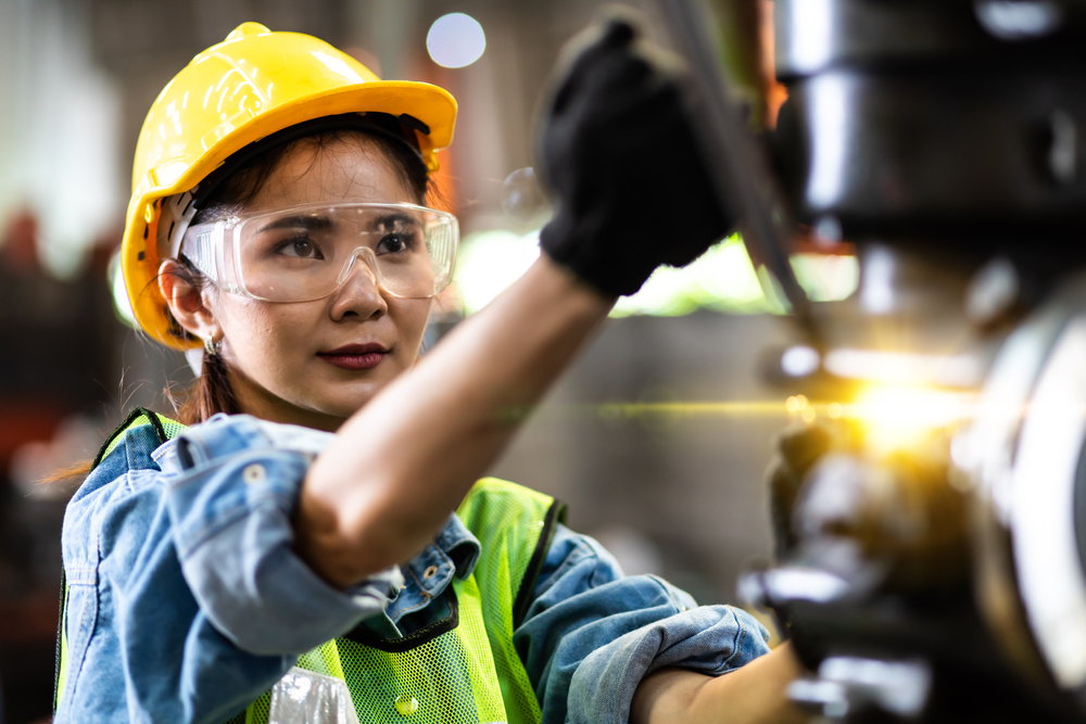 Woman worker wearing safety goggles control lathe machine to drill